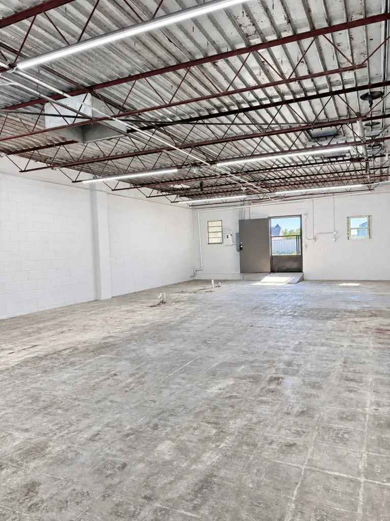 Home Open commercial interior with concrete floor, exposed steel roof trusses, and rear entrance.