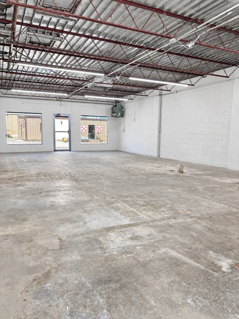 Home Spacious unfinished commercial interior with white walls, concrete floor, and exposed ceiling structure.