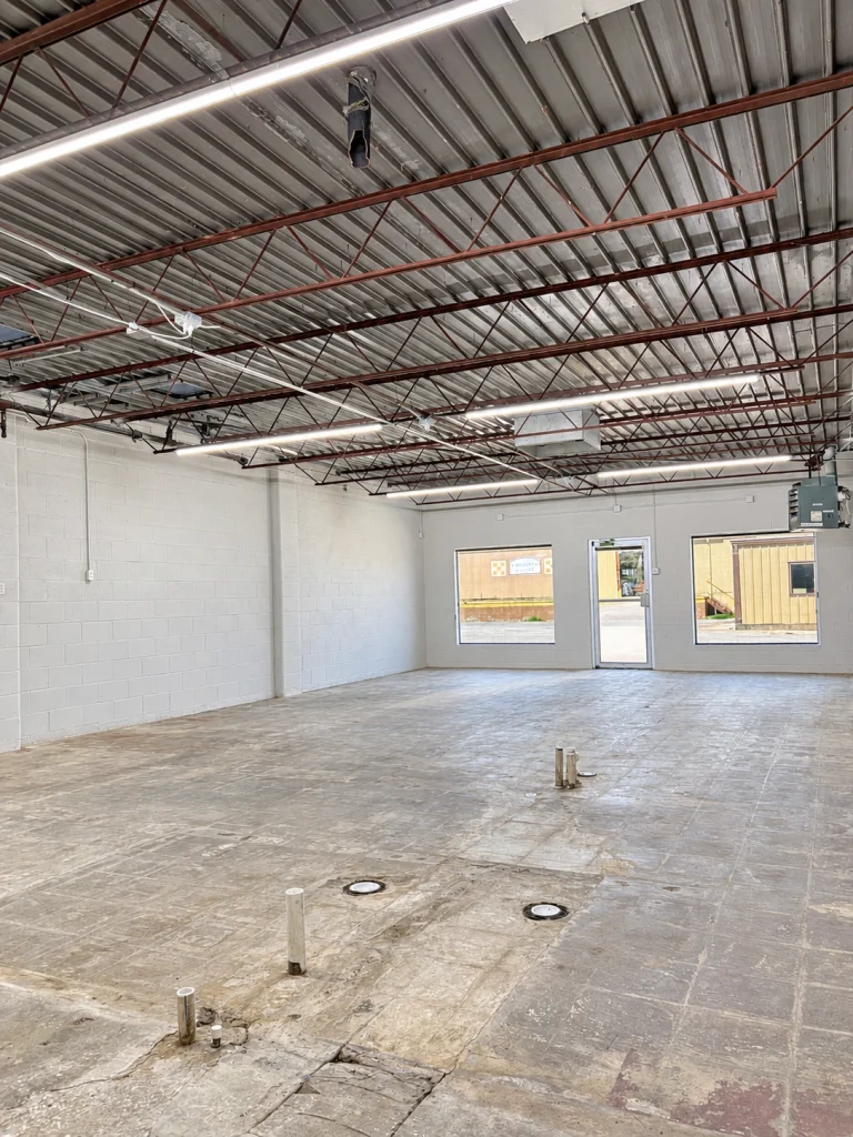 Home Interior view toward the storefront showing open floor space, ceiling trusses, and front windows.
