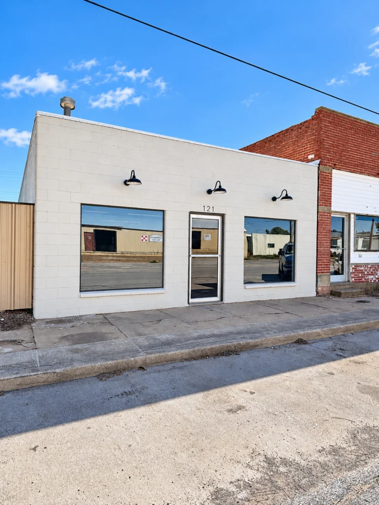 Home Angled view of the commercial building's front facade, large display windows, and sidewalk.